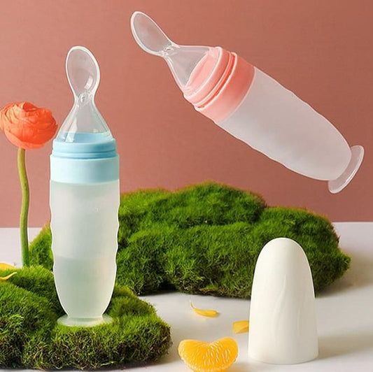 Two baby bottles with spoons on a surface with green grass and flowers.